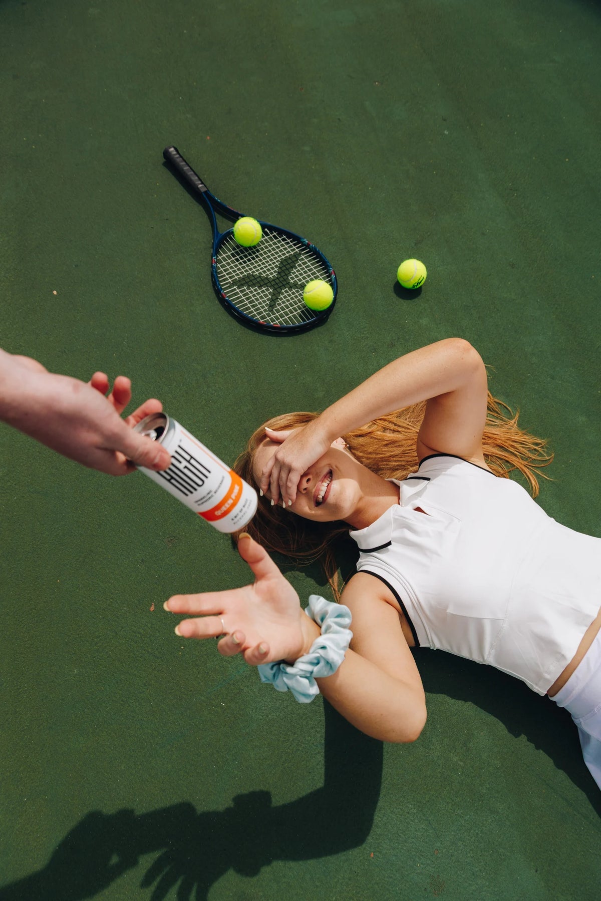 A woman relaxing on a tennis court and reaching for a Queen Pine HIGH can